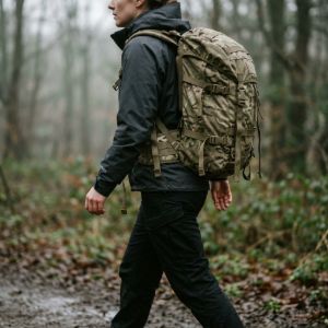 A person wearing a durable military-spec rucksack walks through a misty forest, captured in a cinematic, natural style.