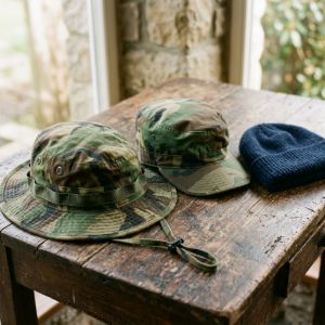 Assortment of military headwear including camouflage boonie hats, patrol caps, and wool beanies on a wooden table.