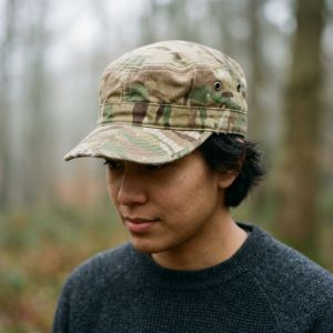 A person wearing a textured British Army MTP combat cap against a soft, misty woodland background.
