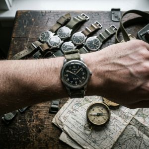 Close-up of a wrist wearing an authentic military field watch with a canvas strap, surrounded by several other vintage-style tactical timepieces.