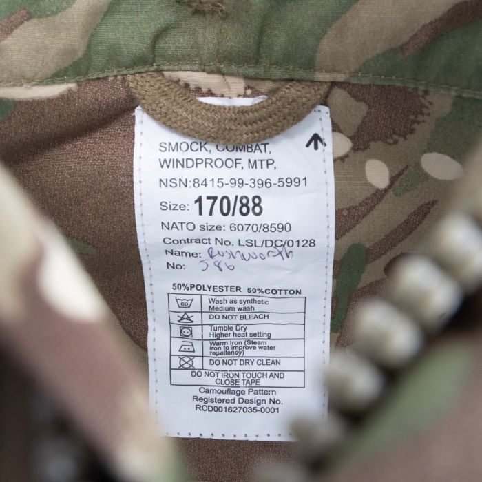 Close-up of British Army military issue label with NSN number, NATO size, and 50/50 polycotton fabric specification