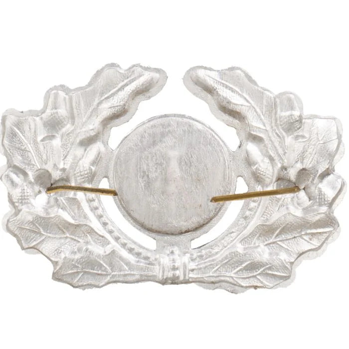 Rear view of DDR NVA visor cap badge showing lightweight stamped aluminum surface and dual bendable brass split-pins
