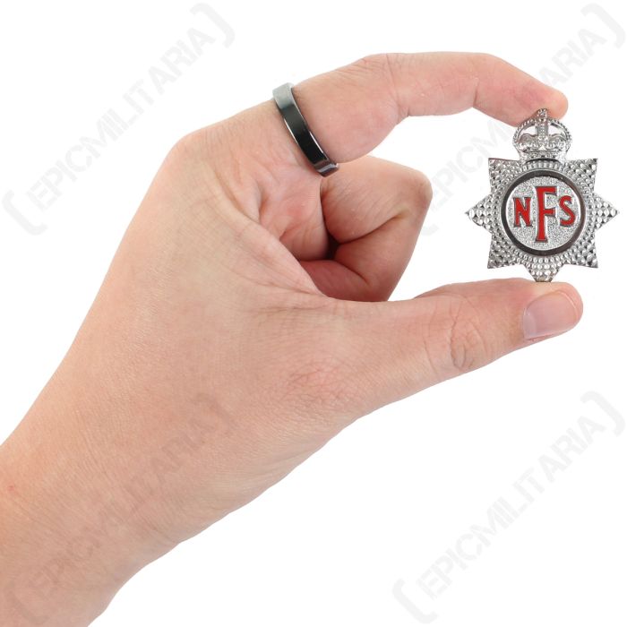 Scale view of original British home front National Fire Service cap badge held between fingers