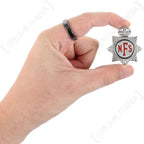 Scale view of original British home front National Fire Service cap badge held between fingers