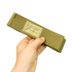 A hand holding a durable olive green British Army combat belt, displaying the size and contract information on a beige label.