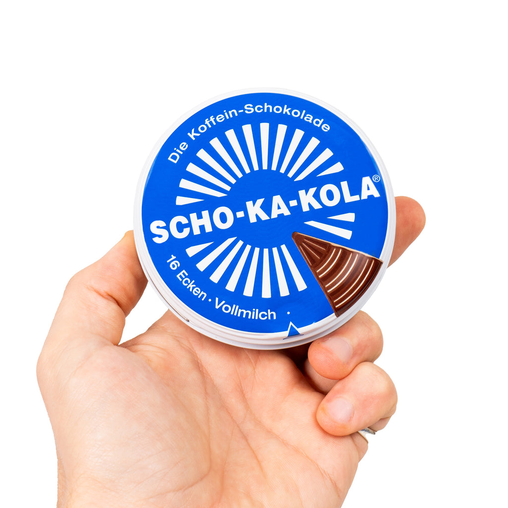 Human hand holding the round blue Scho-Ka-Kola milk chocolate tin, showing its compact size for field rations.