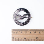 Front of the 40mm circular ATC metal cap badge aligned with a ruler showing its size