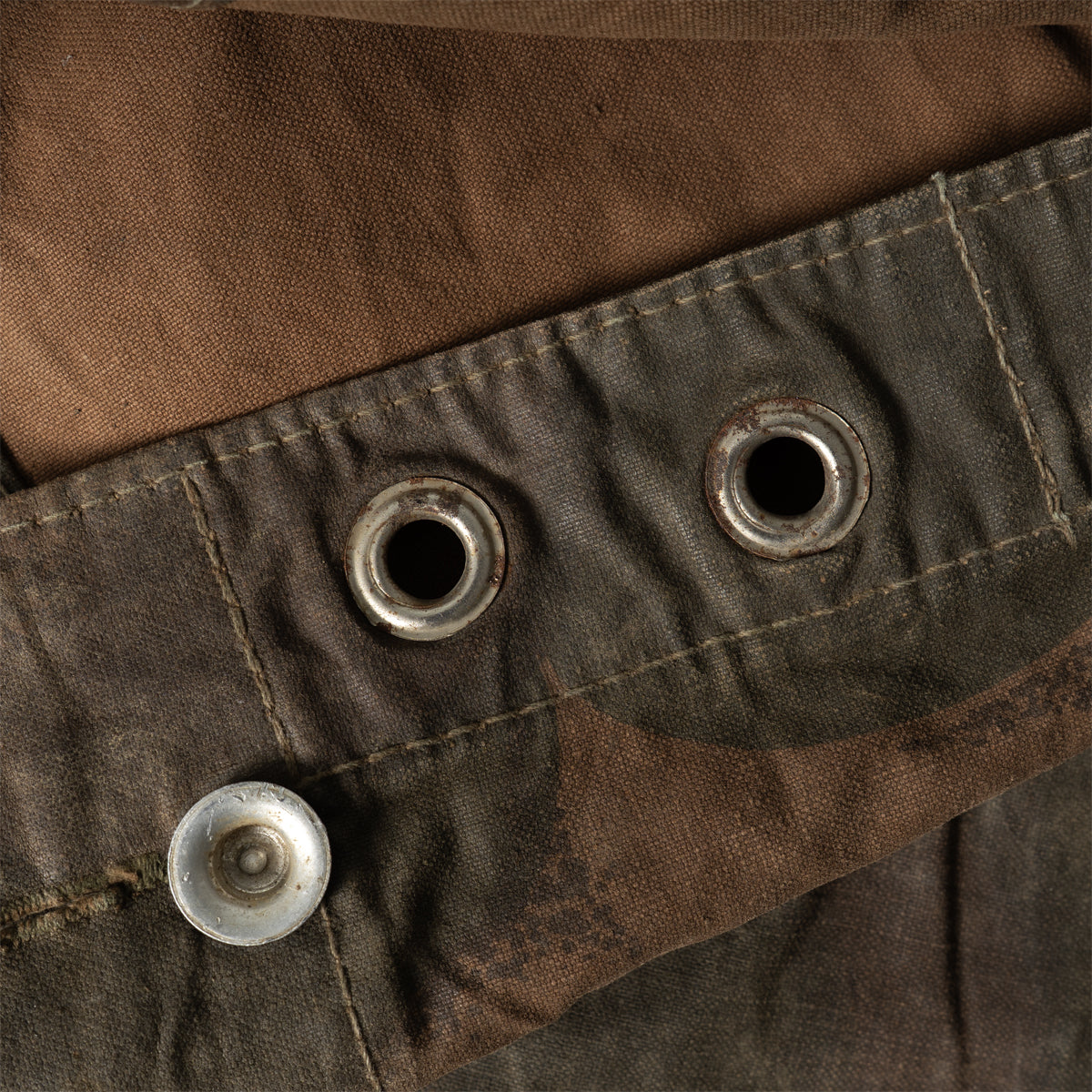 Close-up of the reinforced metal eyelets and aluminium buttons along the edge of the Zeltbahn tarp.