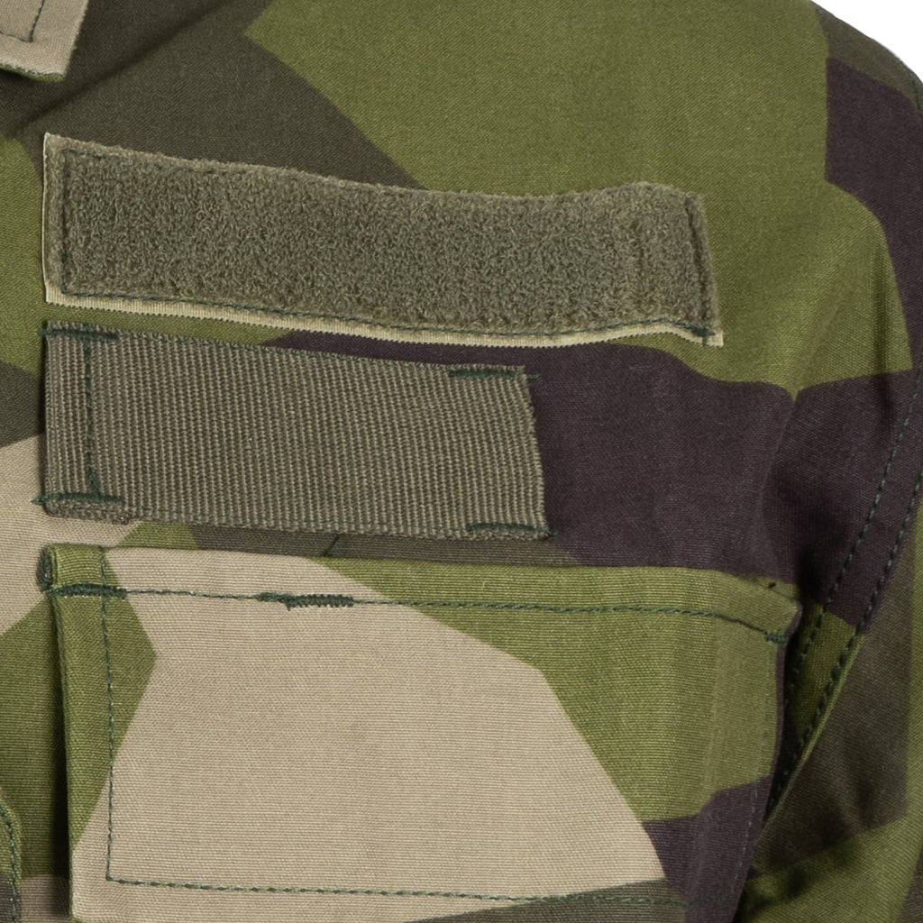 Close-up of the hook-and-loop insignia patches on the chest of the Swedish M90 military field shirt.