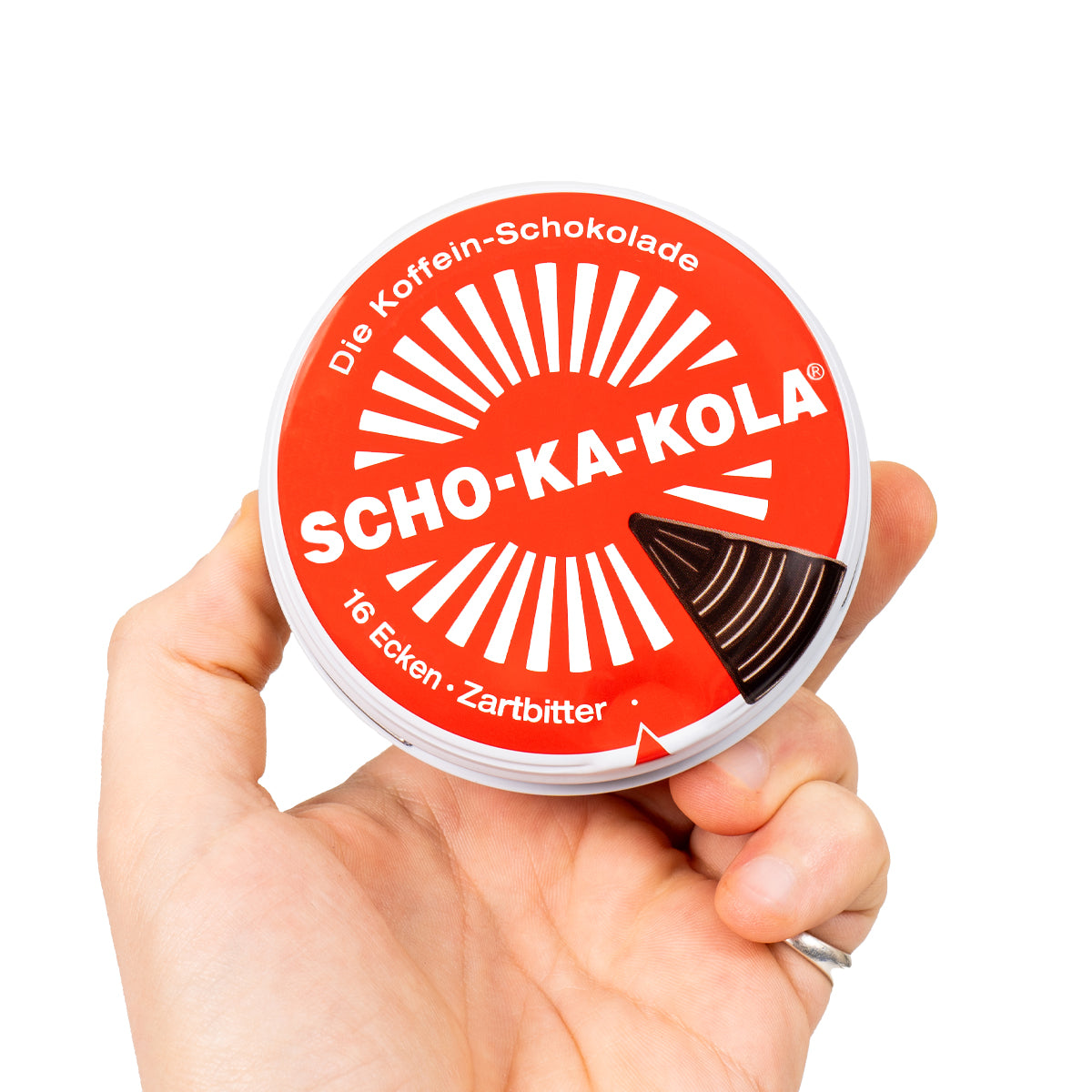 Hand holding a round, iconic red-and-white Scho-Ka-Kola caffeinated dark chocolate tin with a sunburst logo.