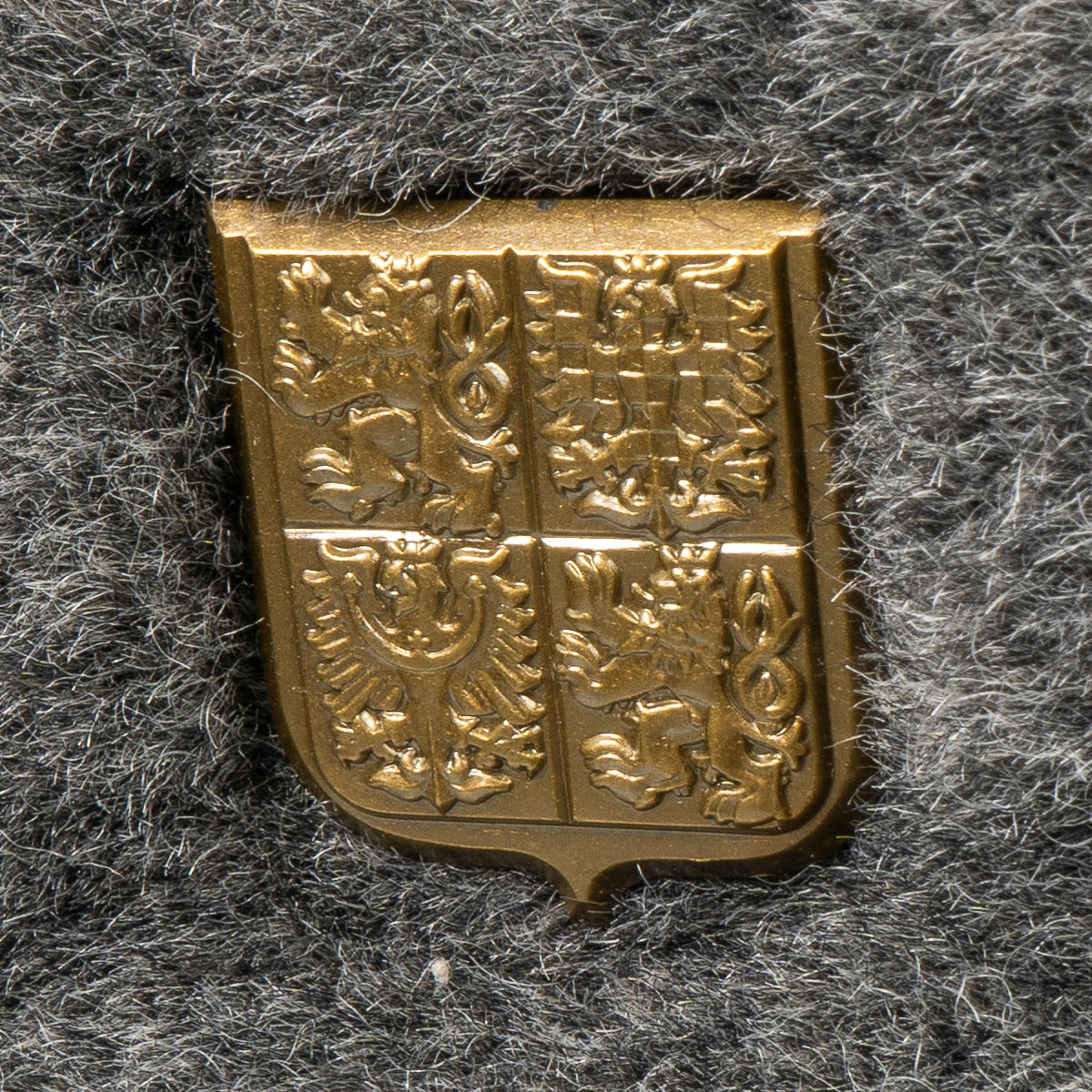 Macro shot of the detailed golden Czechoslovakian cockade emblem mounted on the grey faux fur front of the surplus Ushanka hat.