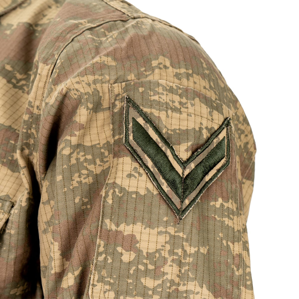 Detailed view of a military rank chevron sewn onto the bicep of a TUBITAK camo ripstop field shirt.