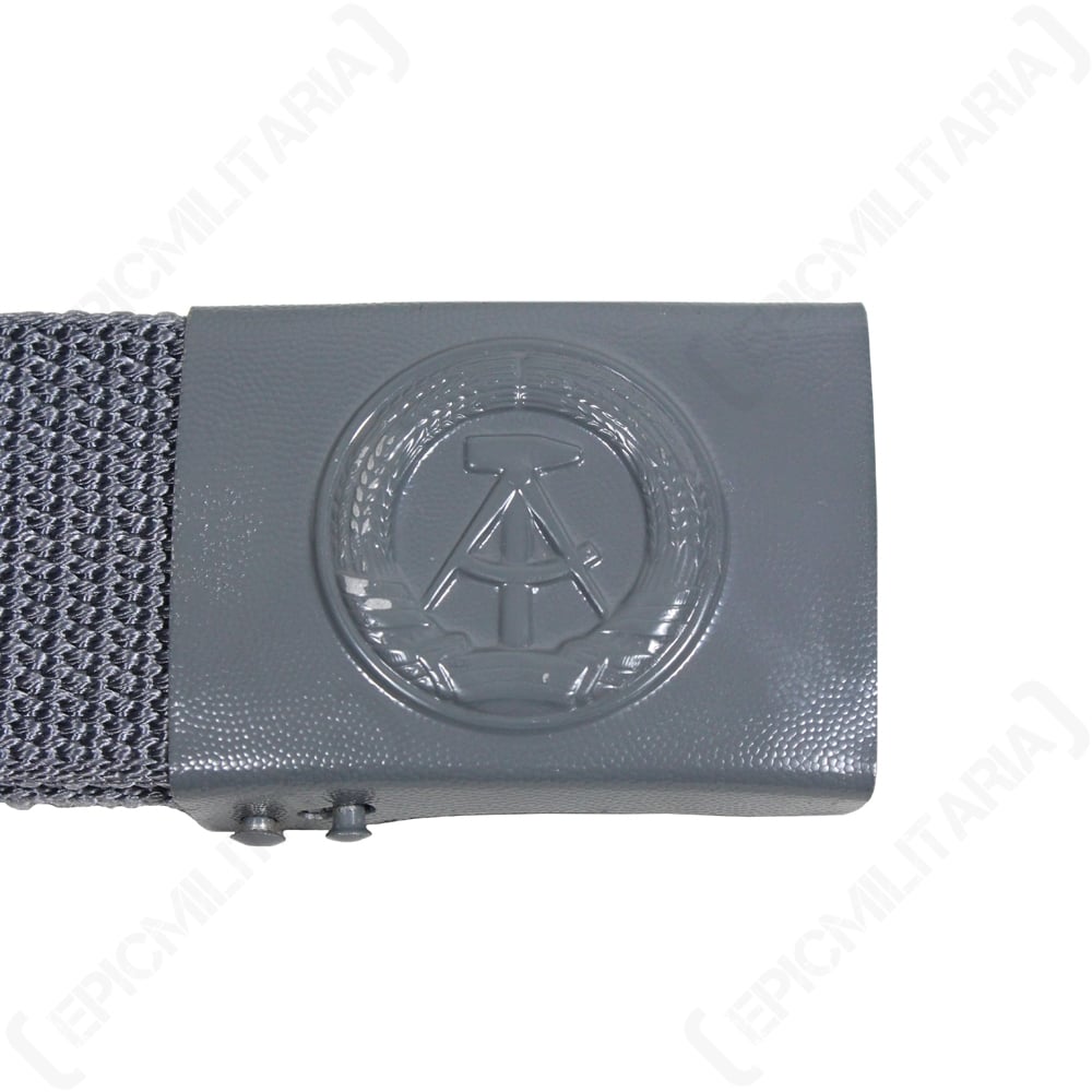 Close-up of the East German NVA belt buckle featuring an embossed hammer and compass symbol on grey metal.