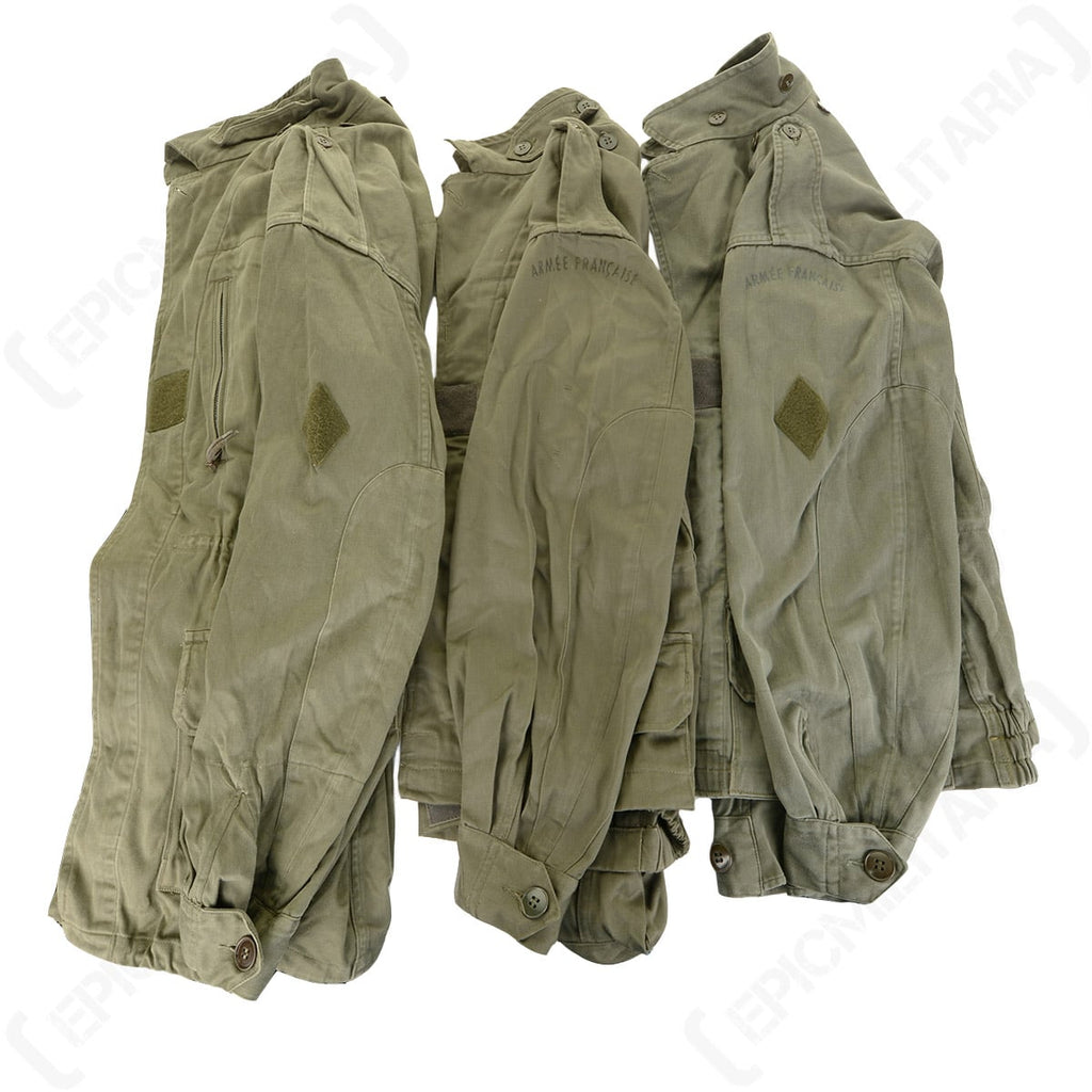 Three original French M64 field jackets stacked to show arm detail, including the Armée Française stamps and hook and loop sleeve patches.