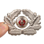 Original East German NVA officer cap badge held in hand showing scale and 5 by 7 cm size