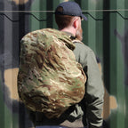 Close-up side view of a person wearing a daypack protected by an MTP camouflage cover, showing the secure elasticated fit.