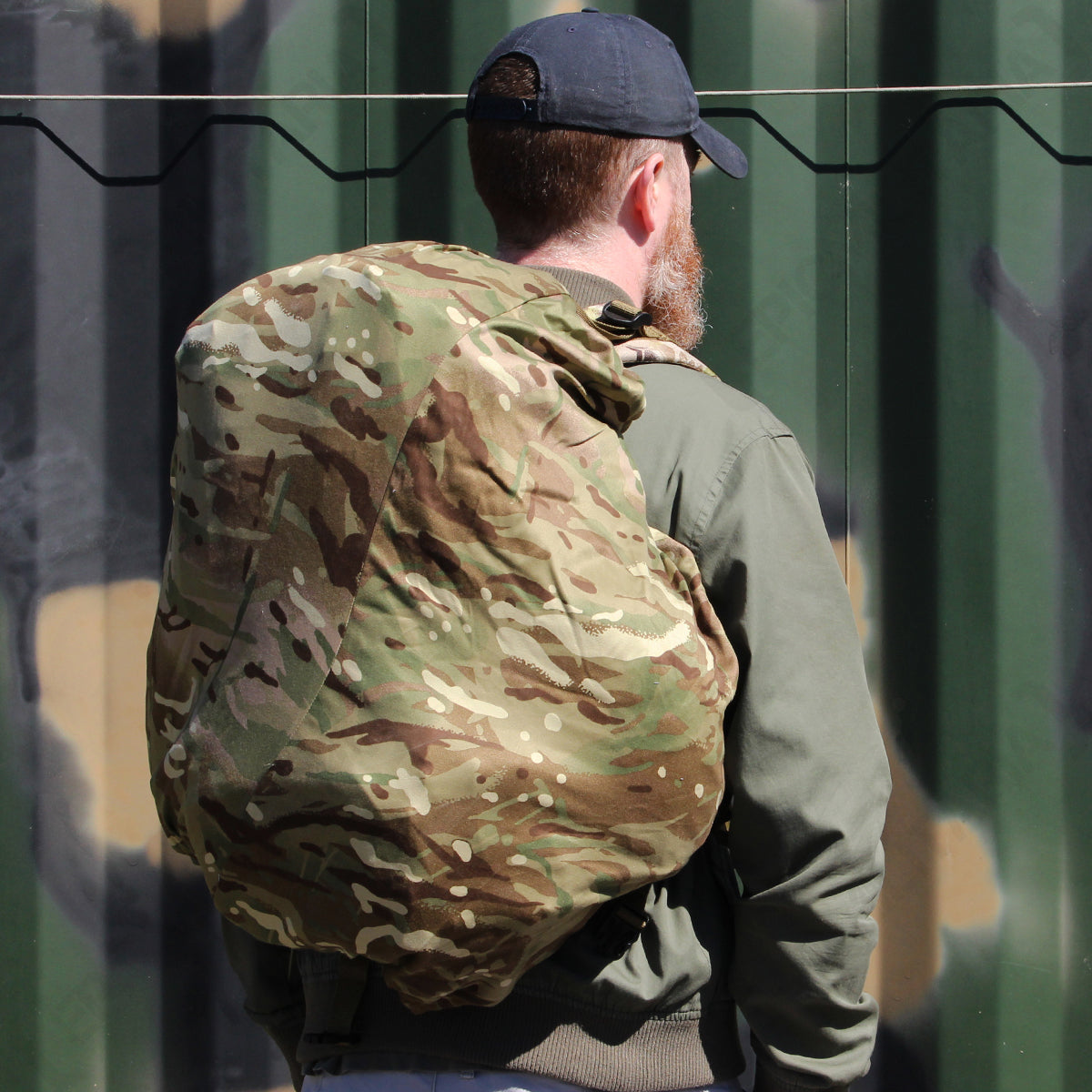 Close-up side view of a person wearing a daypack protected by an MTP camouflage cover, showing the secure elasticated fit.