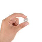 A person holding a single 18mm silver metal dish button between their thumb and index finger to demonstrate the small, versatile scale.