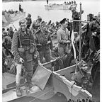 Black and white historical wartime photograph showing soldiers on a landing craft wearing traditional British cap comforters.