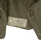 Close-up of the official WWII US Army M43 field jacket hood laundry tag with original printed instructions and military branding.