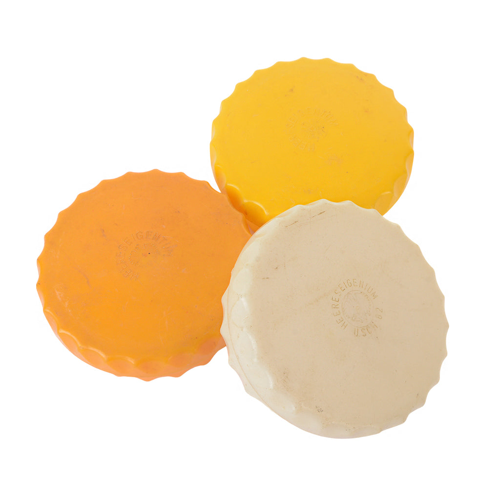 Three original Austrian Army butter dishes in orange, yellow, and cream plastic with scalloped bottle-cap style edges.