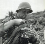 Black and white historical photograph of a soldier using a traditional metal mess tin in the field.