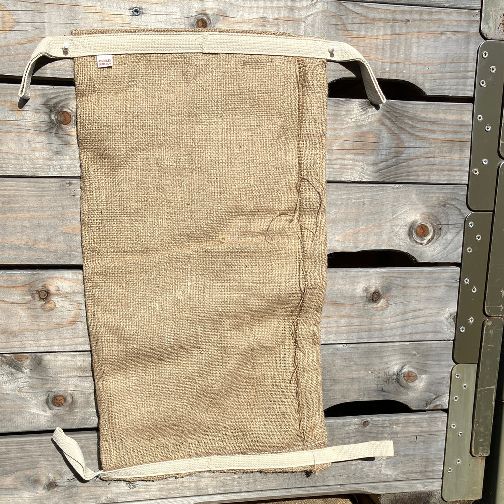 A flat, empty Dam It Up flood defence bag laid vertically against a rustic wooden surface, highlighting the durable jute material and integrated cotton pull tabs.