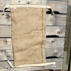 A flat, empty Dam It Up flood defence bag laid vertically against a rustic wooden surface, highlighting the durable jute material and integrated cotton pull tabs.