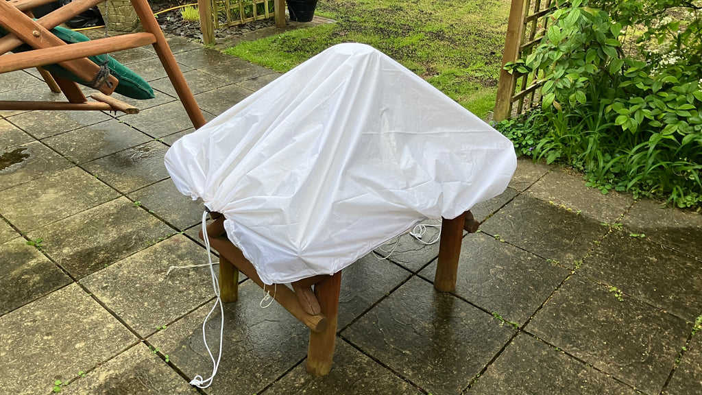 White waterproof utility sheet draped over a garden wooden stool to provide weather protection.