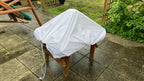 White waterproof utility sheet draped over a garden wooden stool to provide weather protection.