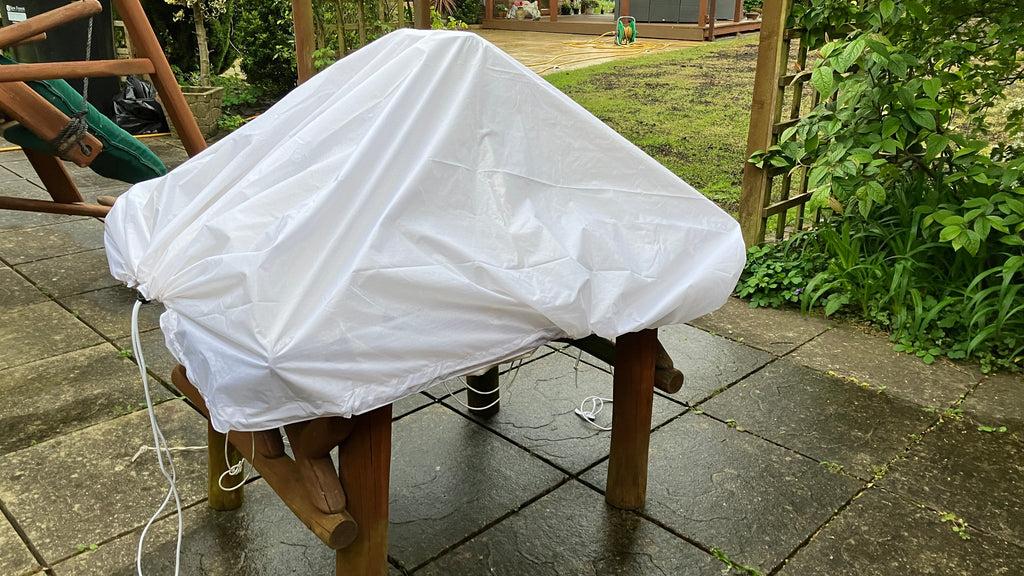 High angle view of a white waterproof utility sheet secured over a wooden outdoor stool with its elasticated cord.
