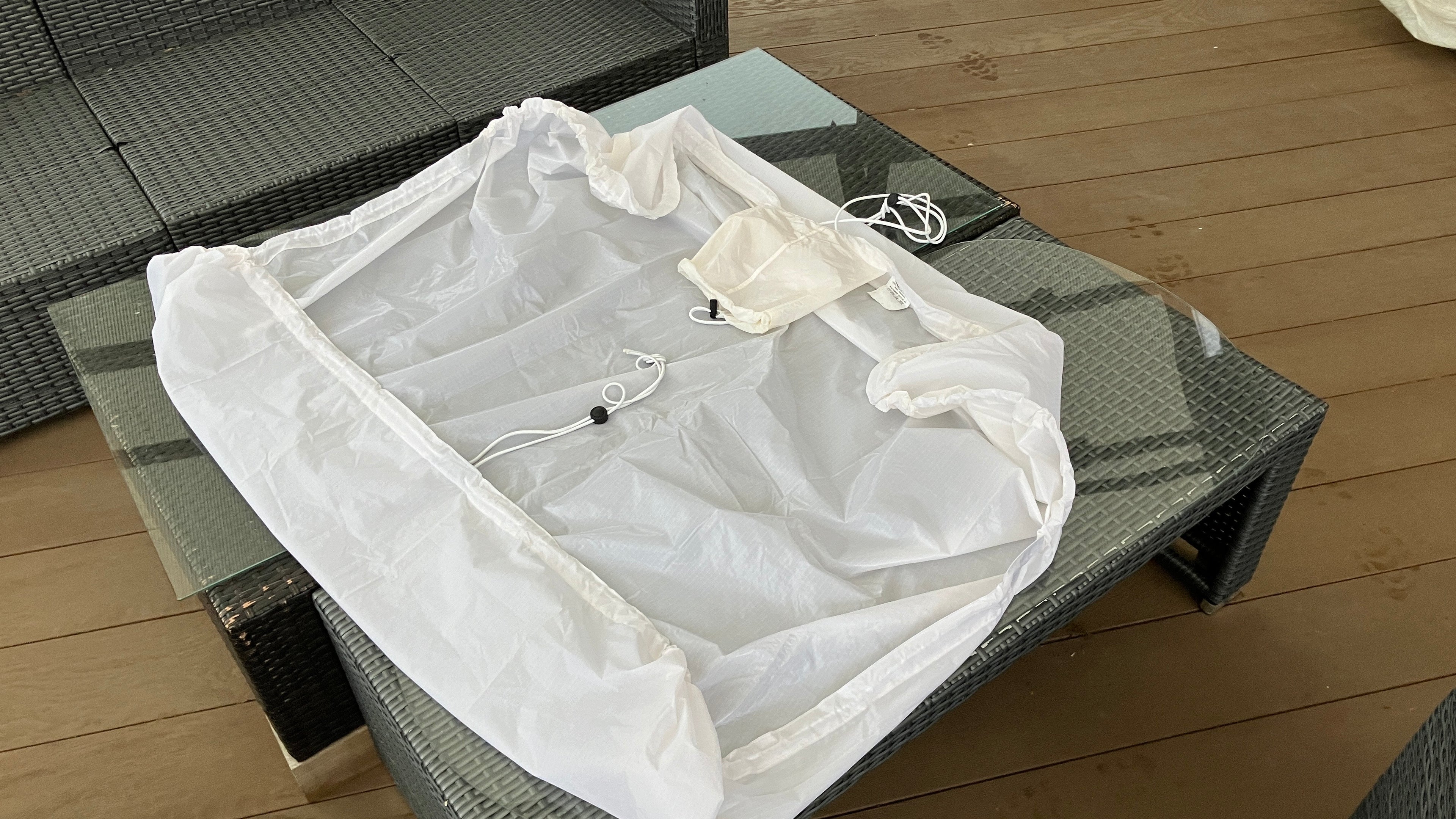 A white utility sheet with an elasticated perimeter and built-in storage pouch laying flat on a textured table.