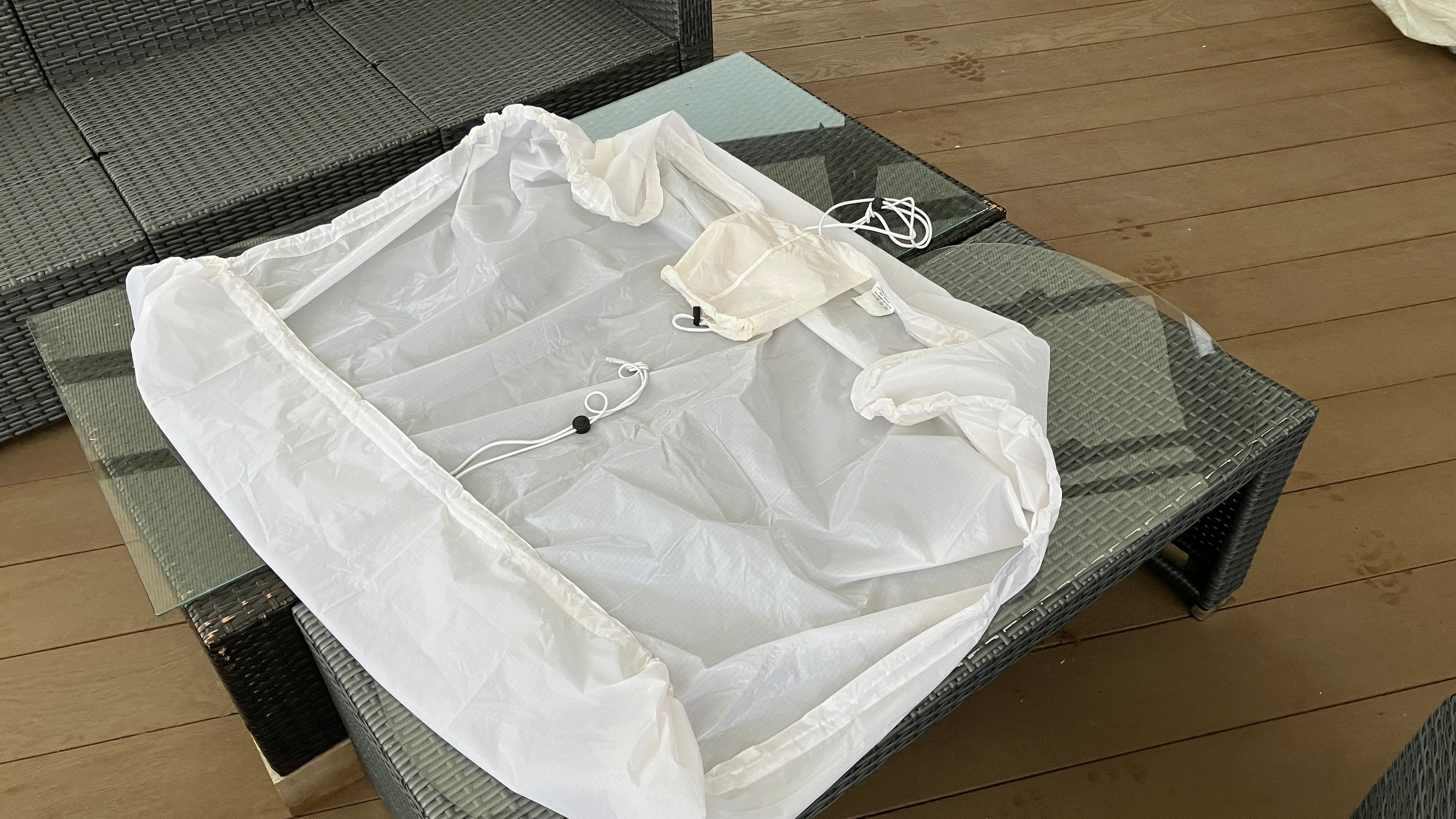 A plain white protective utility sheet laid flat on a table, featuring an elasticated hem and integrated storage pocket.