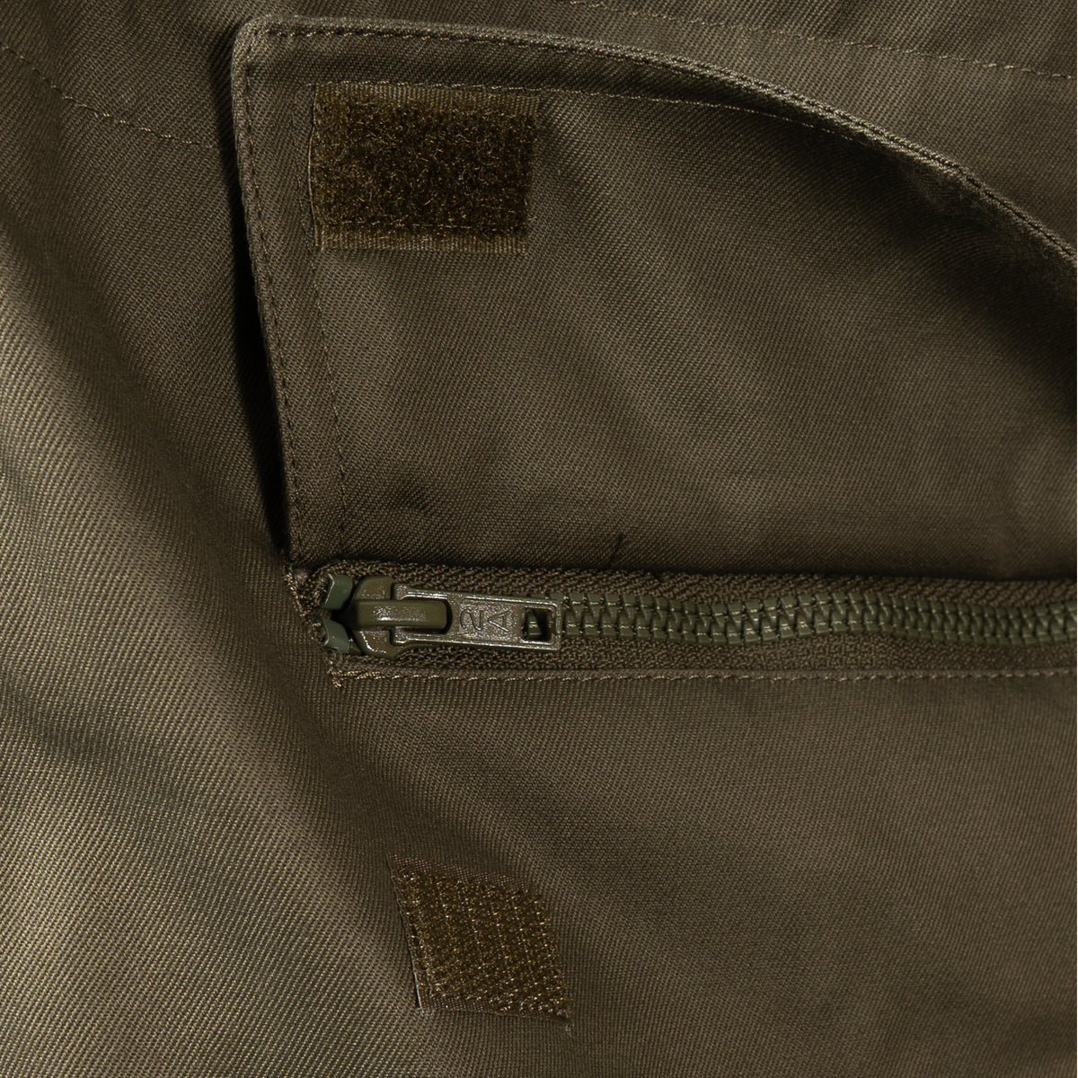 Detail view of a secure zippered waist pocket with robust construction on the military parka.
