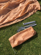 Tent fabric, poles, and metal pegs laid out for packing into the included nylon bag.
