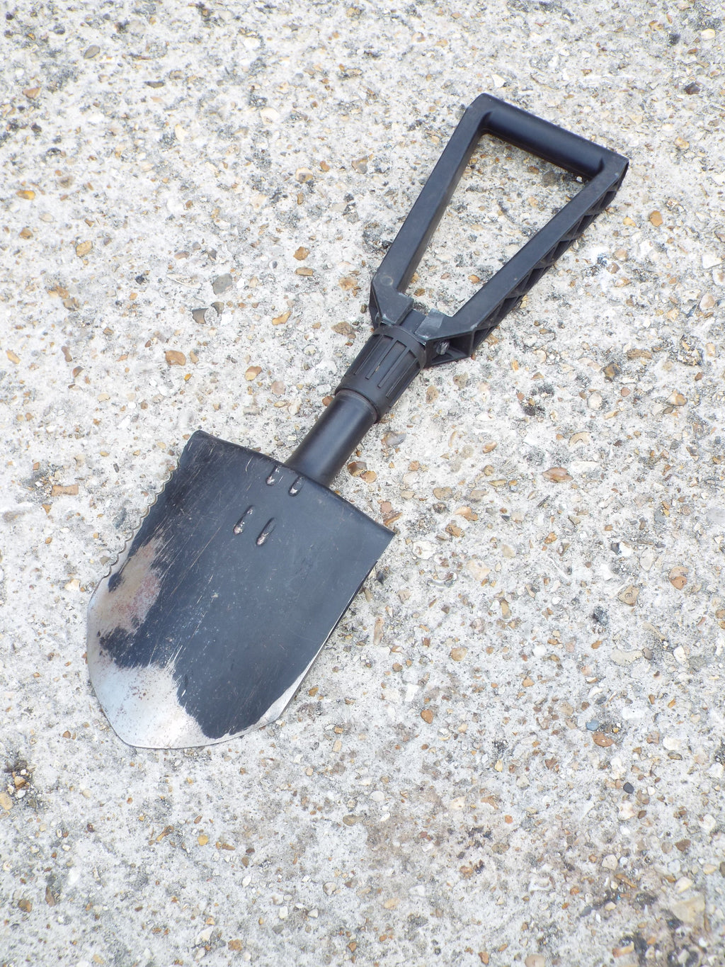 Full view of the military surplus Gerber entrenching tool showing the steel blade with signs of use and the black handle.