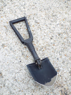 US Army Gerber E-Tool folding shovel in full shovel configuration with black steel blade and nylon handle on textured ground.