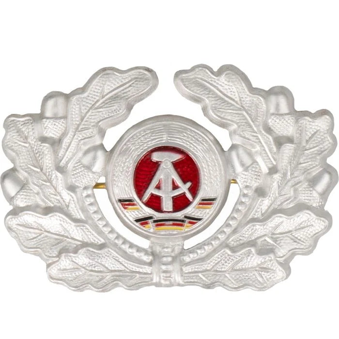 Front view of original East German NVA DDR EM cap badge showing silver oak leaves and central painted hammer and compass emblem