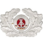 Front view of original East German NVA DDR EM cap badge showing silver oak leaves and central painted hammer and compass emblem