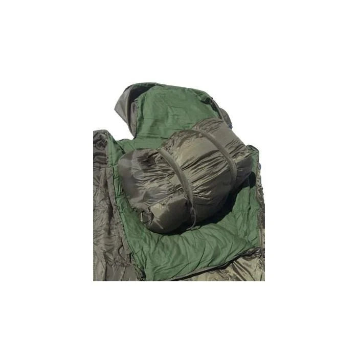 Mil-Tec Pilot sleeping bag rolled up and secured with elastic straps inside its integrated carry bag, showing the olive green interior liner.