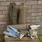 Collection of three East German strichtarn camo tent pole pouches, two standing upright and one open on a wooden crate, displaying wooden poles, metal pegs, and rope.