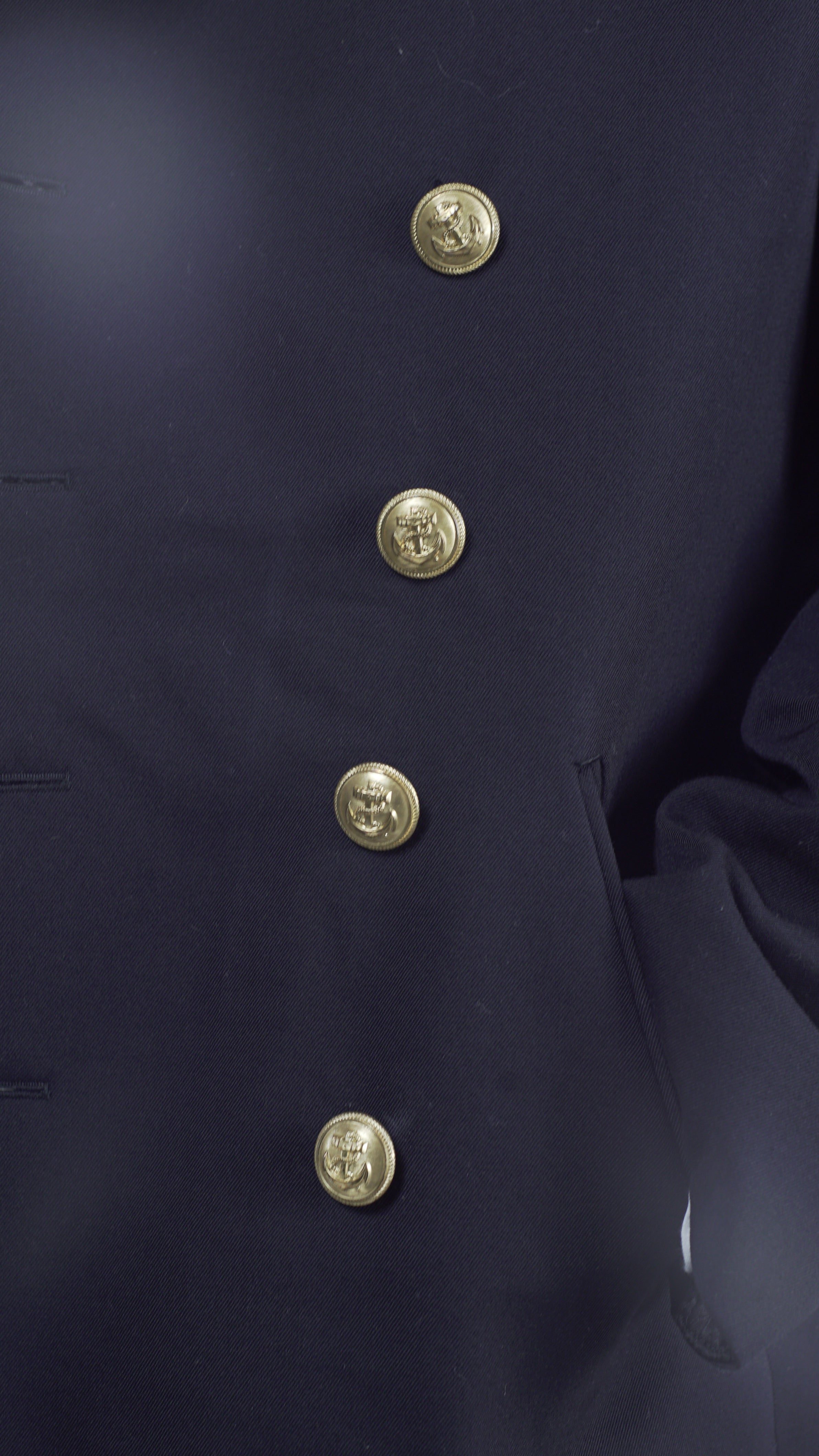 Close-up detail of the gold anchor emblem buttons on the black gabardine fabric of a German Navy peacoat.