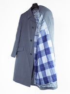 Close-up of the grey gabardine trench coat partially open to display the warm, removable plaid liner and single-breasted buttoning detail.