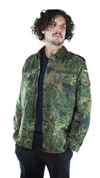 Man wearing a genuine German army surplus flecktarn camo shirt featuring a buttoned front and classic camouflage pattern.