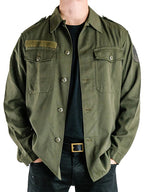 Close-up front view of a vintage Austrian army olive combat shirt with dual breast pockets, epaulets, and a velcro strip.