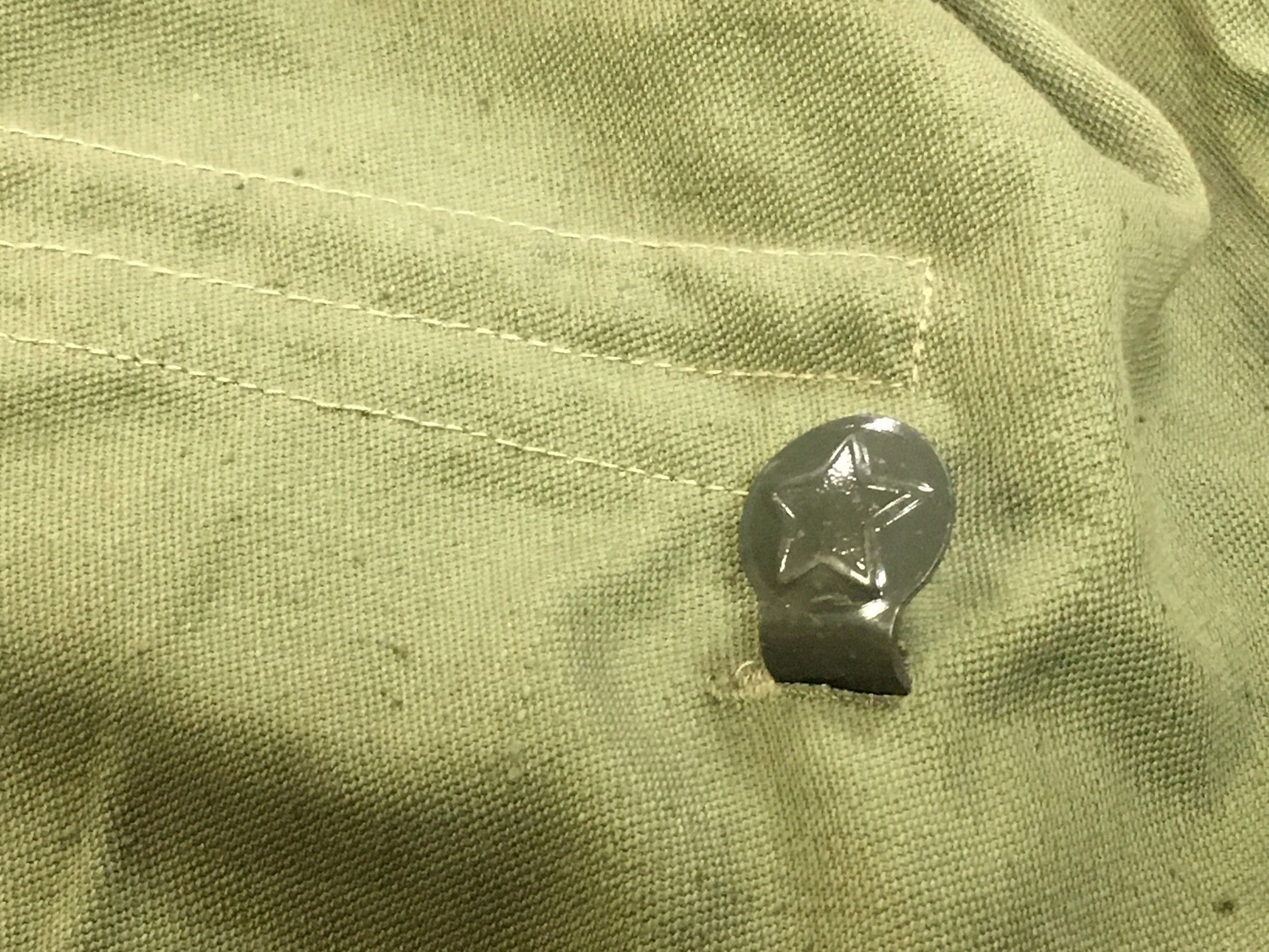 Detailed view of a metal waist hook embossed with the socialist star on a Bulgarian military shirt.