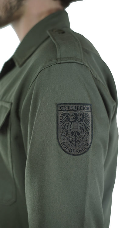 Detailed close-up of the Austrian army insignia patch on the sleeve of a genuine vintage olive green combat shirt.