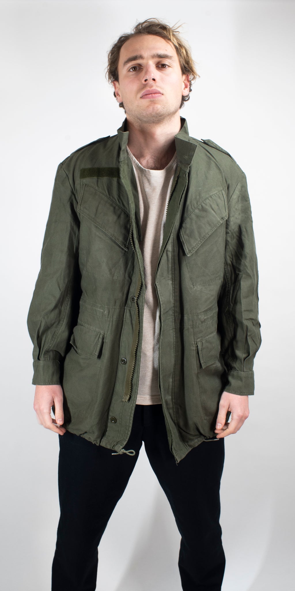 Front view of a man wearing a heavy duty cotton canvas Belgian military surplus field jacket in olive green with multiple utility pockets.