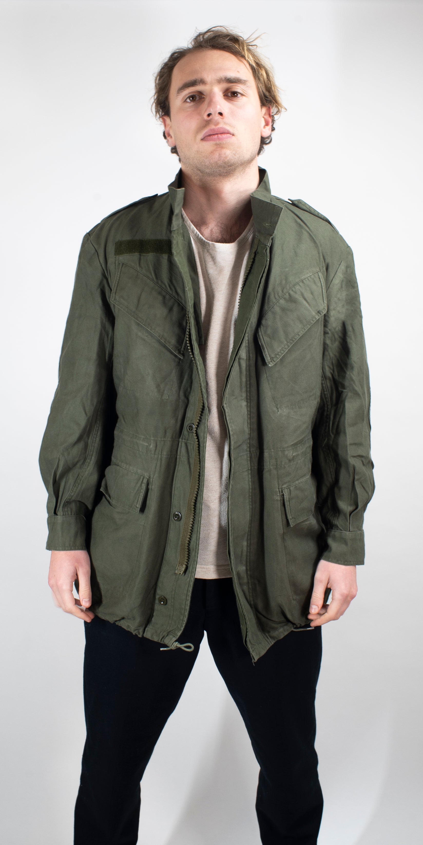 Front view of a man wearing a heavy duty cotton canvas Belgian military surplus field jacket in olive green with multiple utility pockets.