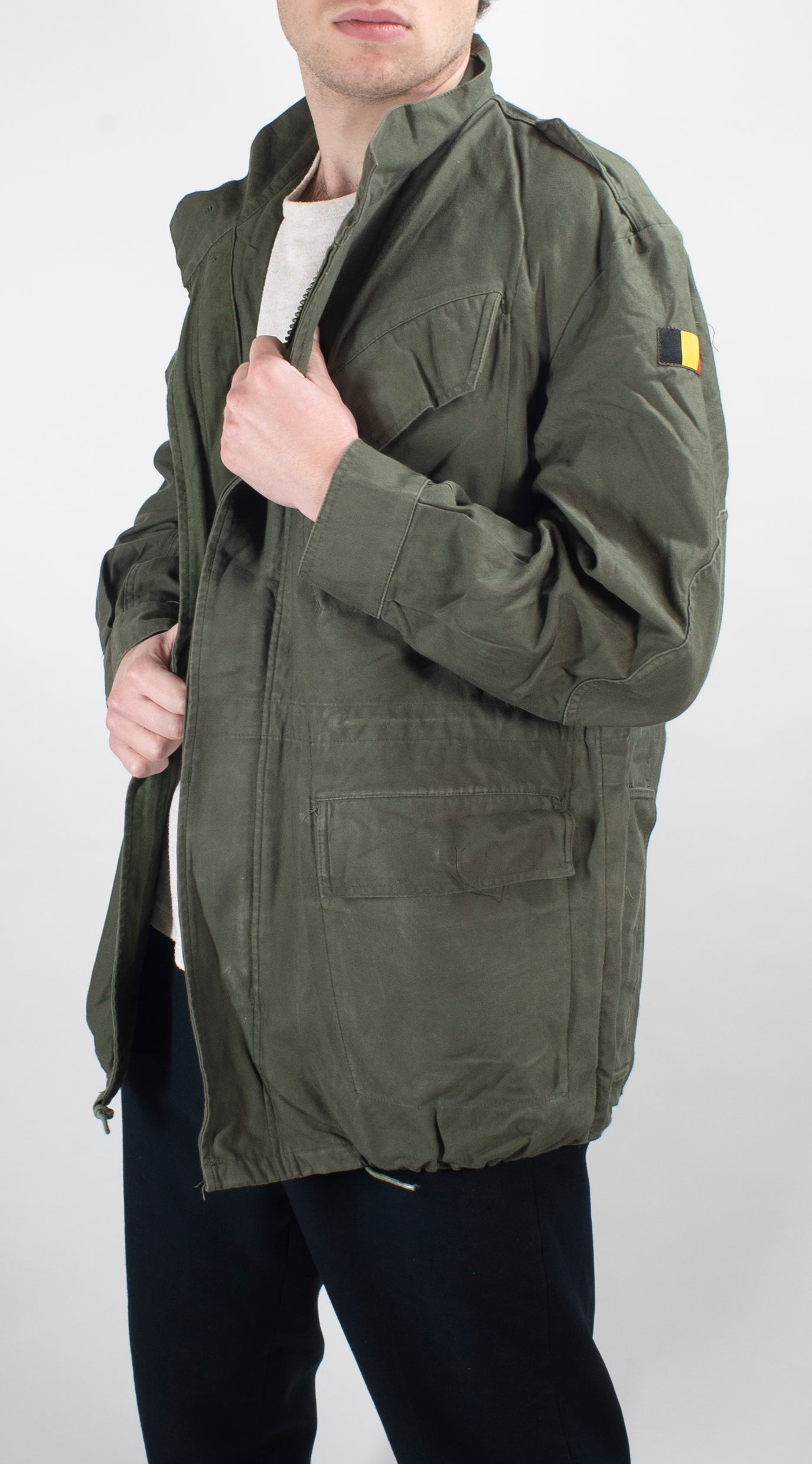 Side profile of the olive green Belgian field jacket highlighting the sturdy construction, adjustable cuff, and visible Belgian shoulder flag badge.